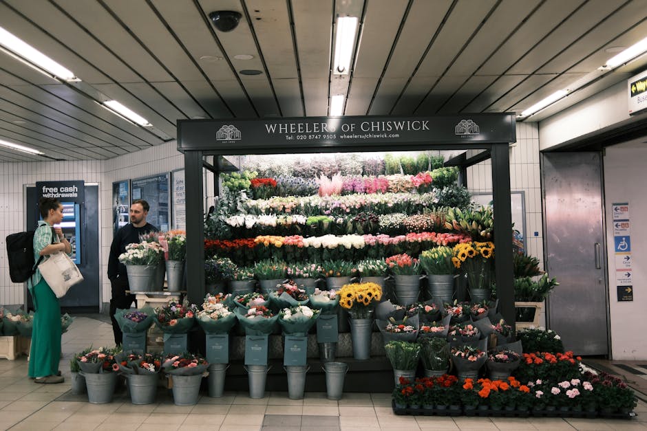 A vibrant floral display at Wheeler of Chiswick flower stall in an underground station, featuring an array of fresh flowers including roses, tulips, chrysanthemums, and carnations in various colors su